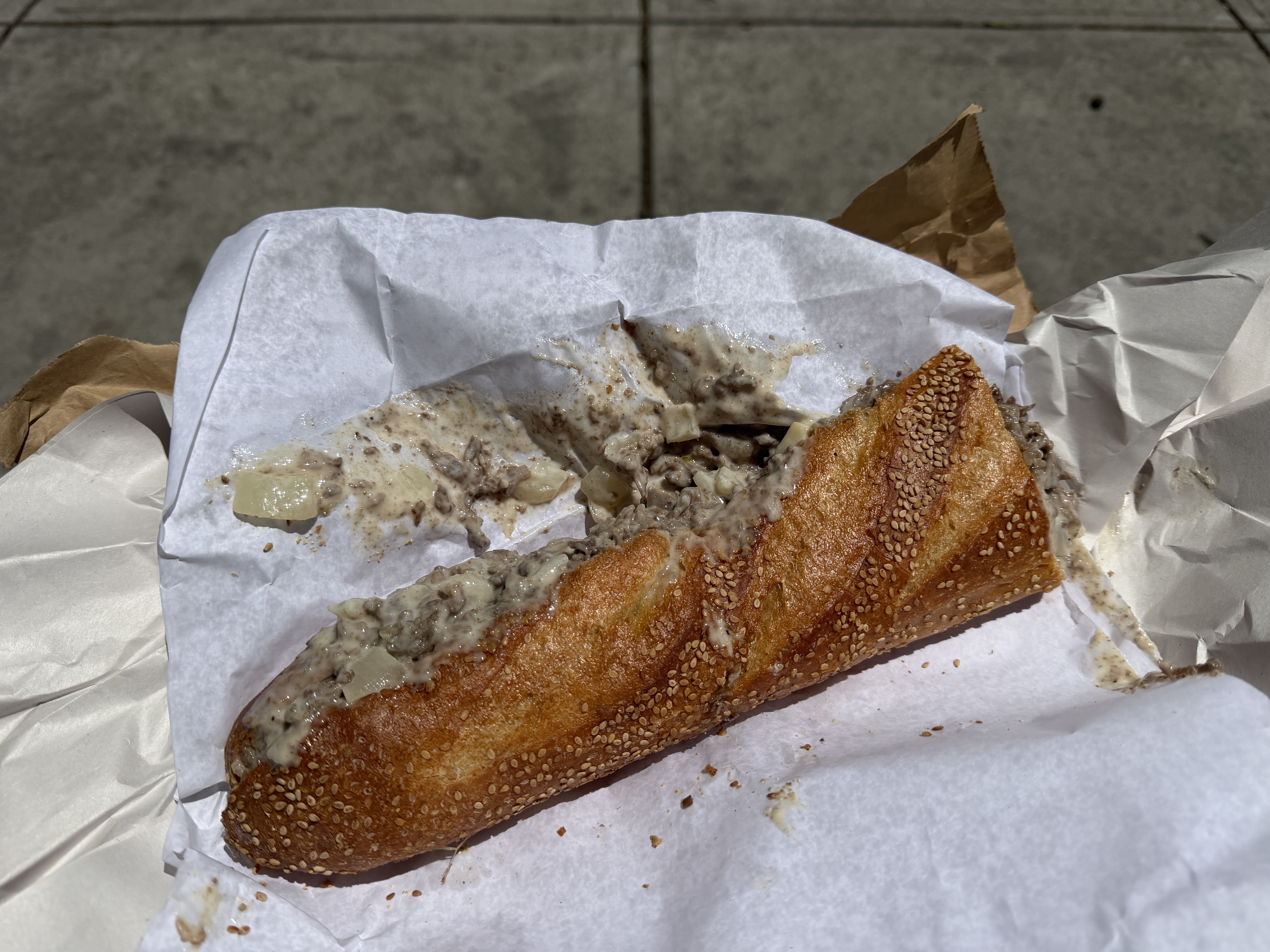 A Philly cheesesteak from Angelo&rsquo;s Pizzeria in Philadelphia. Served on their classic sesame roll, it has chopped beef, Cooper sharp cheese, and onions. It&rsquo;s all sitting on several layers of thick paper.
